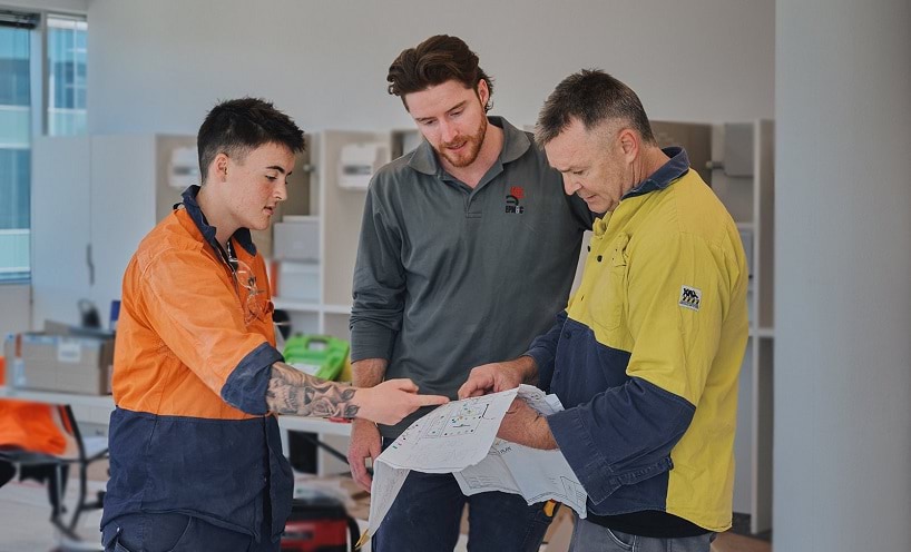Apprentice electricians at work Two apprentice electricians at work with their supervisor discussing plans